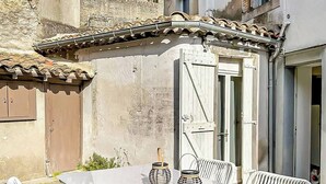 A glass-top table with white chairs, a door, and a stone wall in the background. - Le Petit Rempart, T2 vue sur remparts de la Cité (Carcassonne)