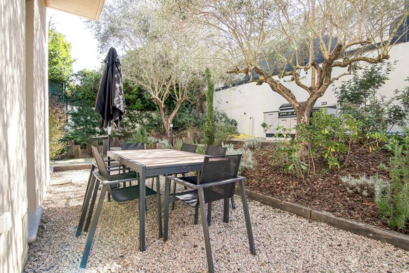Une terrasse extérieure avec une table et des chaises, entourée de gravier et de plantes.