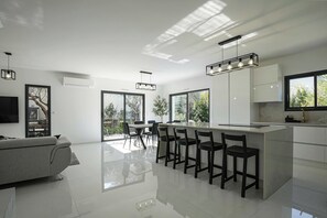 A modern kitchen with a central island, large windows, and a dining area with chairs.