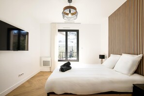 A modern bedroom with a bed, a TV mounted on the wall, a window with a view, and a wooden slat wall.
