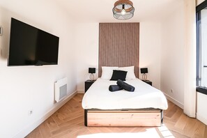 Une chambre à coucher moderne avec un lit, des tables de chevet, un téléviseur fixé au mur et une fenêtre.