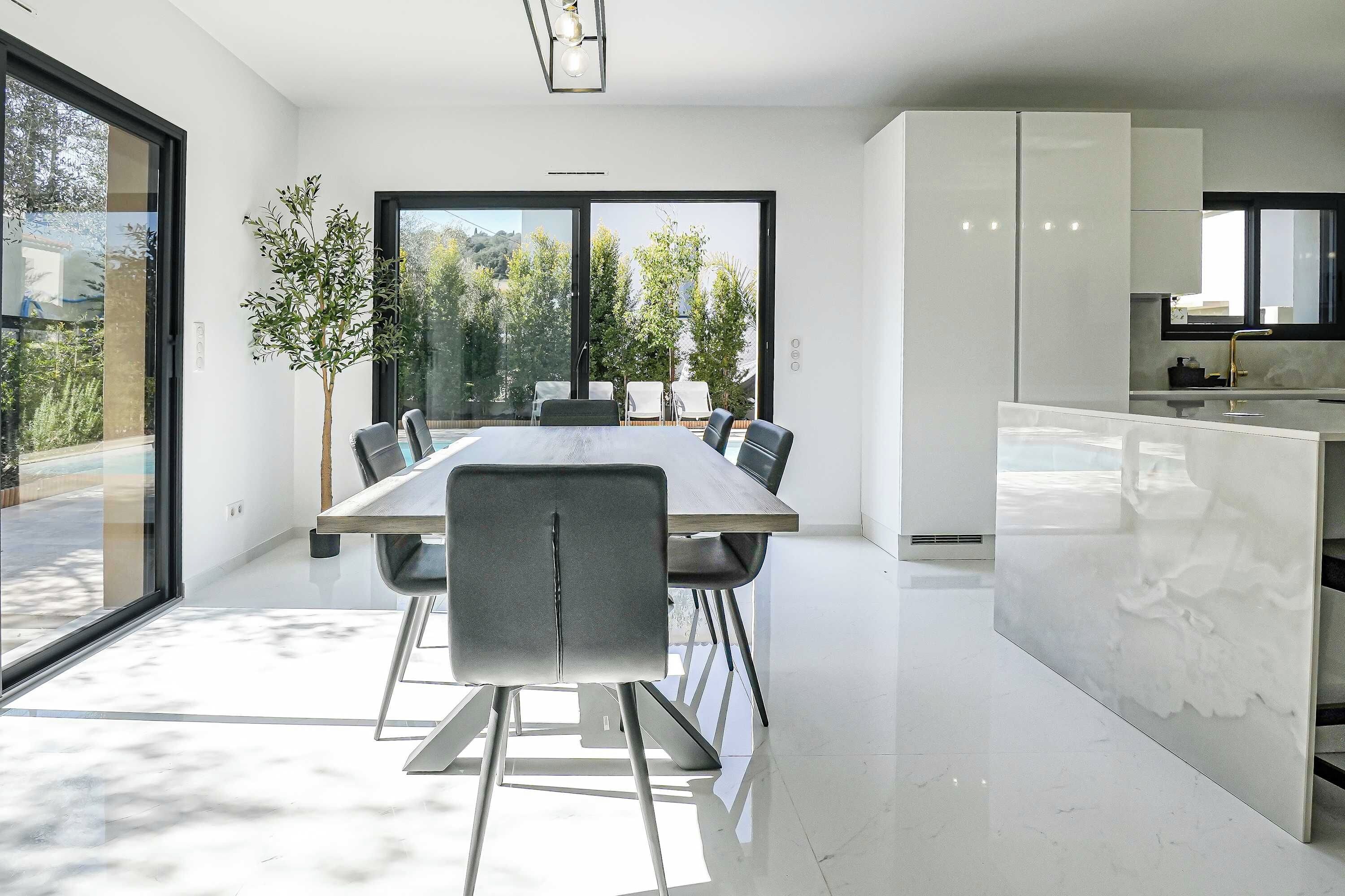 A modern kitchen with white cabinets, a marble countertop, and a large window overlooking a garden.