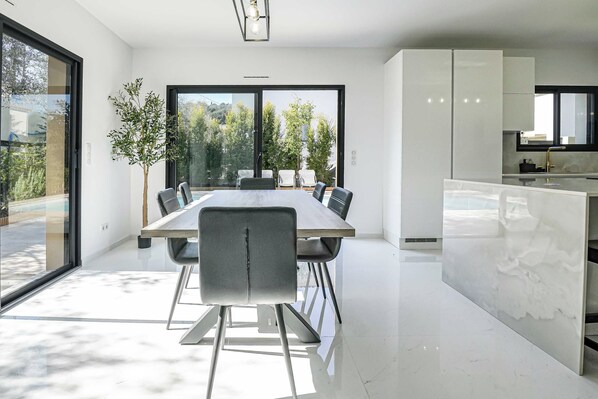 A modern kitchen with white cabinets, a marble countertop, and a large window overlooking a garden.