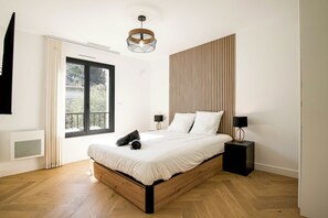 A modern bedroom with a wooden bed, a large window, and a unique wall panel design. - LX133 Villa jardin, piscine privée et calme absolu (Villeneuve-Loubet)