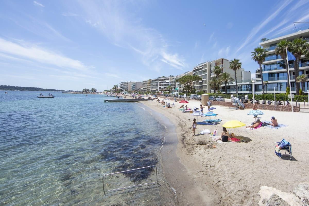 A beach with clear water, umbrellas, and buildings in the background.