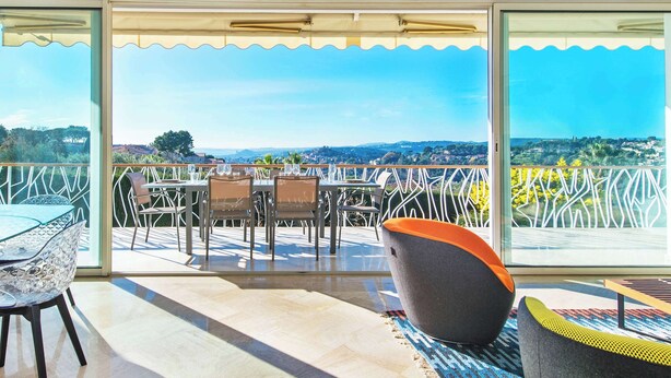 A balcony with a glass table and chairs, a large potted plant, and a view of the landscape.