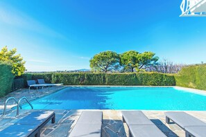 Una piscina con sillas de descanso y cielo despejado.