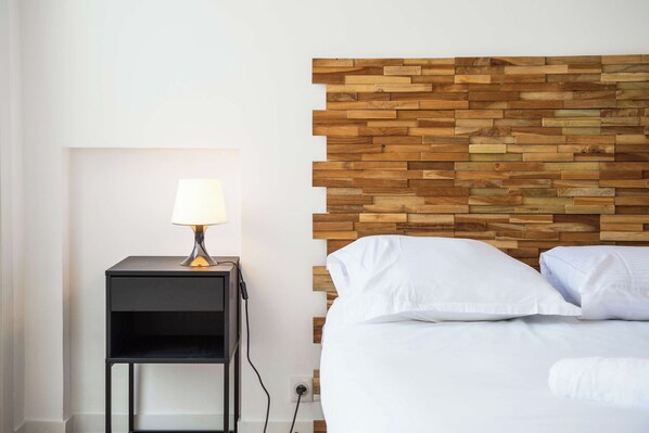 A neatly made bed with white linens, a bedside table with a lamp, and a wooden headboard.