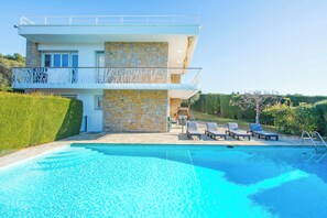 A modern two-story house with a swimming pool, stone walls, and a balcony with white railings.