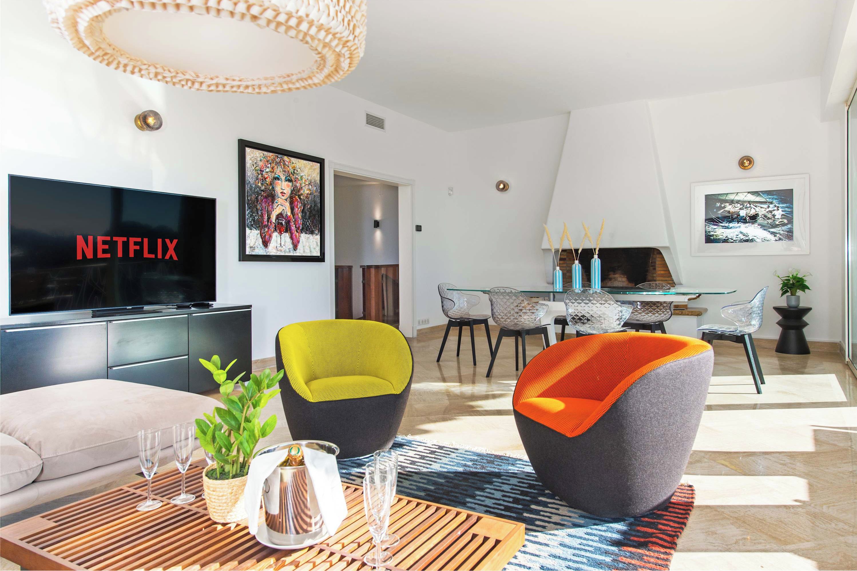 A modern living room with a flat-screen TV, comfortable seating, a dining area, and artwork on the walls.