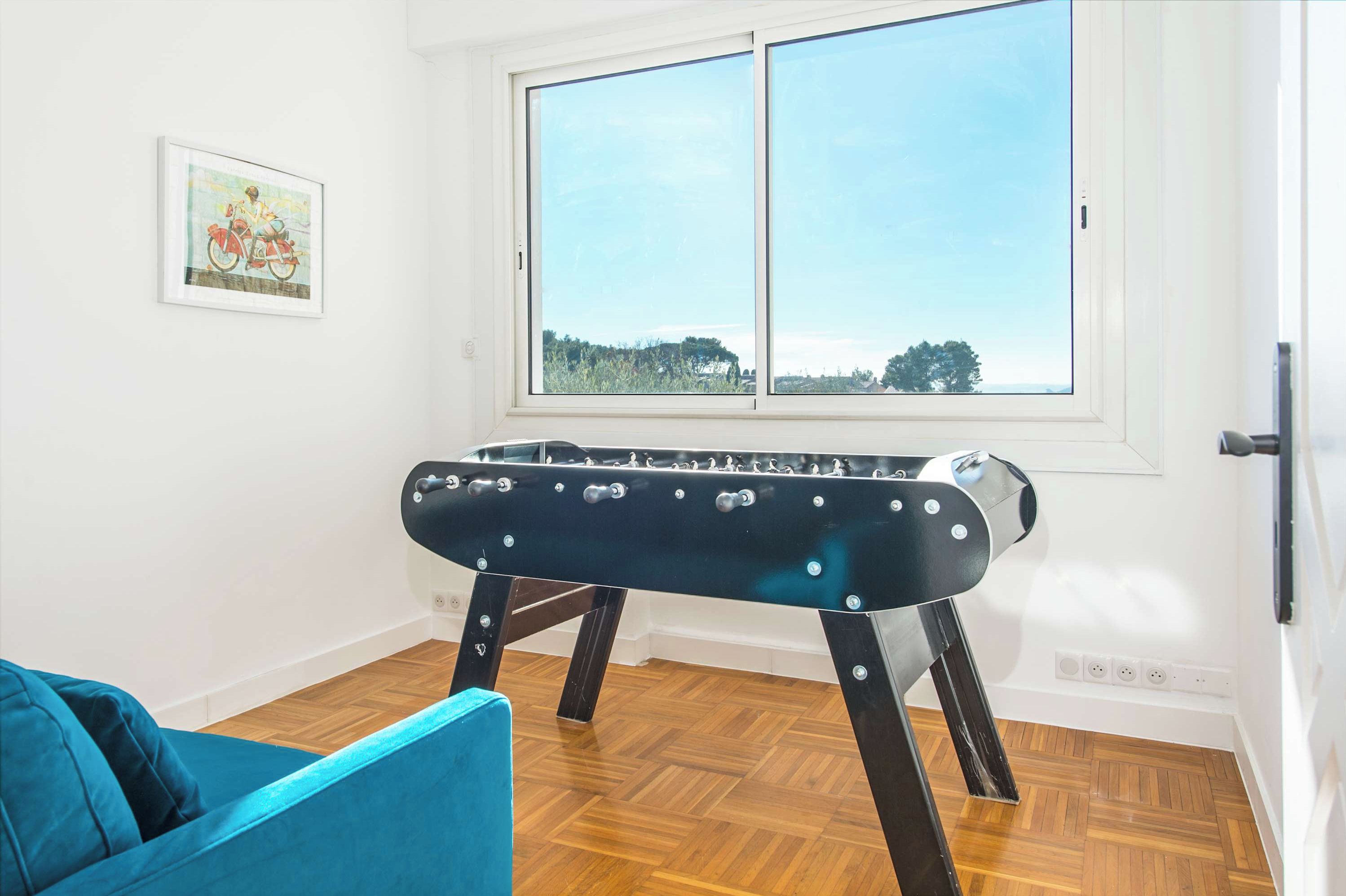 A room with a foosball table, a blue sofa, and a window with a view of trees.