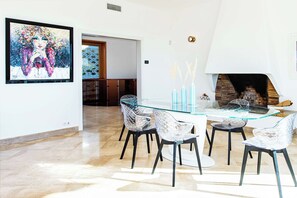 A modern dining area with a glass table and chairs, a fireplace, and a framed painting on the wall.