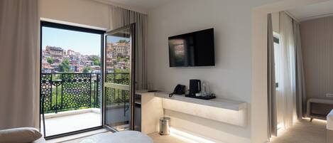 A modern hotel room with a balcony, a flat-screen TV, a small table, and a sofa.