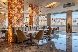 A modern restaurant with marble columns, leather seating, and large windows offering city views.