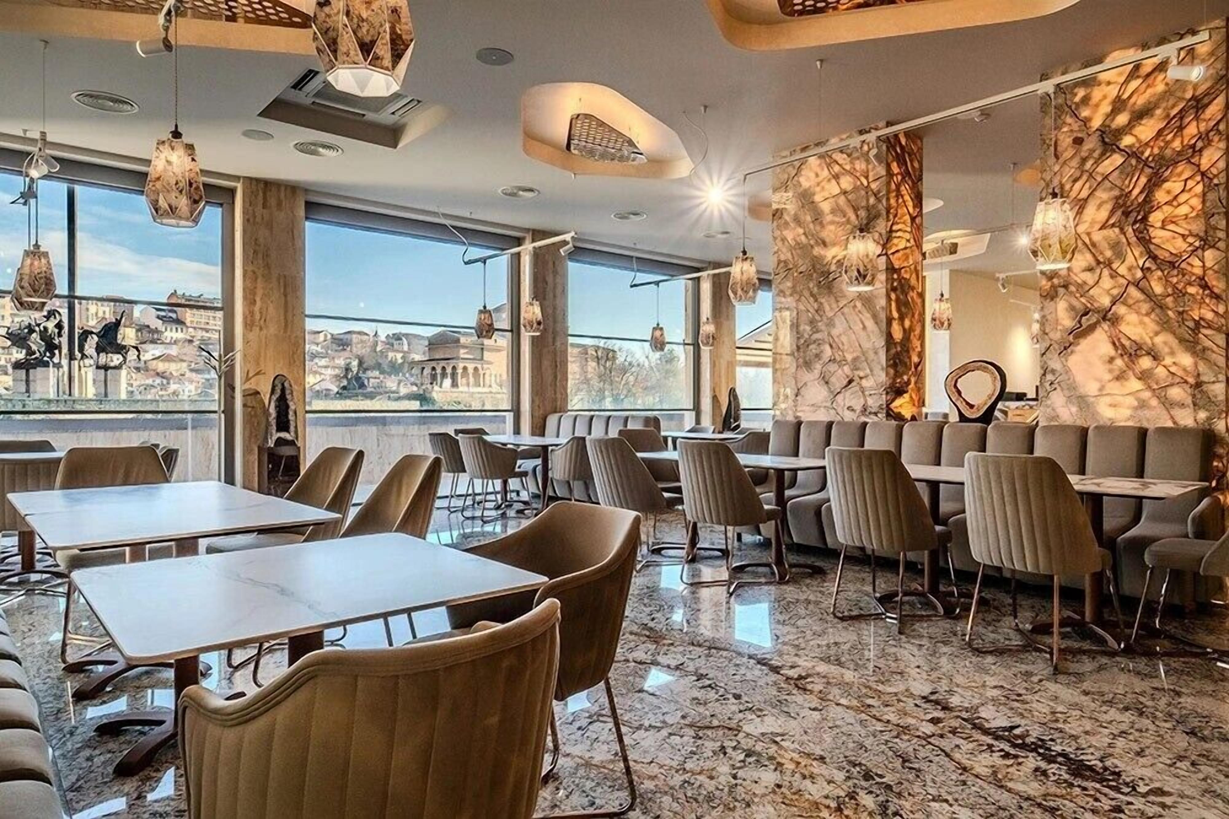 Un restaurante moderno con suelo de mármol, amplias ventanas con vistas a la ciudad y mobiliario contemporáneo.