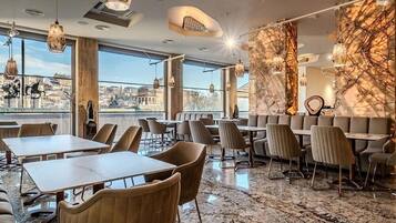 Un restaurante moderno con suelo de mármol, amplias ventanas con vistas a la ciudad y mobiliario contemporáneo.