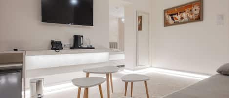 A modern hotel room with a flat-screen TV, a coffee maker, a mini-fridge, a sofa, and a painting on the wall.
