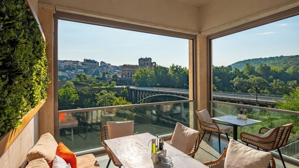 Un balcón con vista a un puente y edificios, amoblado con una mesa y sillas.