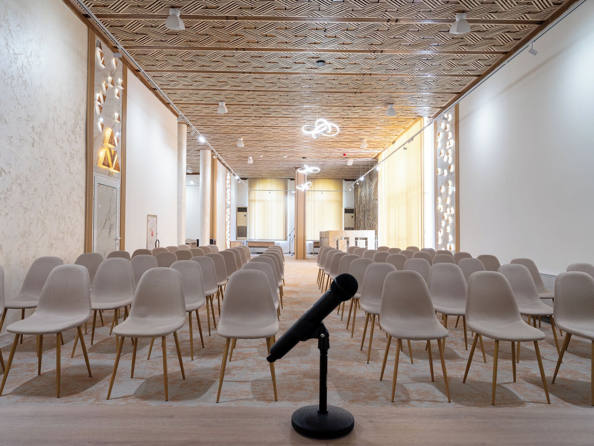 A conference room with rows of chairs, a podium, and a patterned ceiling.
