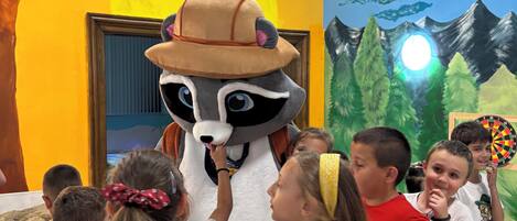 A room with a mural of a sunny landscape, a raccoon mascot, and children interacting.