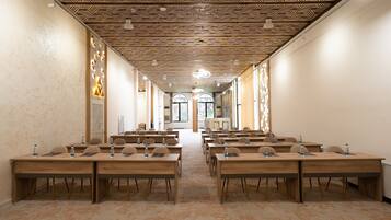 A conference room with multiple tables and chairs, a patterned ceiling, and large windows at the end.