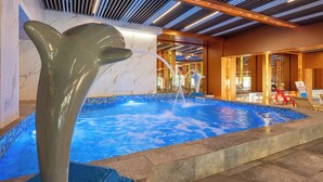 Una piscina con una escultura de delfín, un techo con diseño de listones y una zona de bar con sillas.