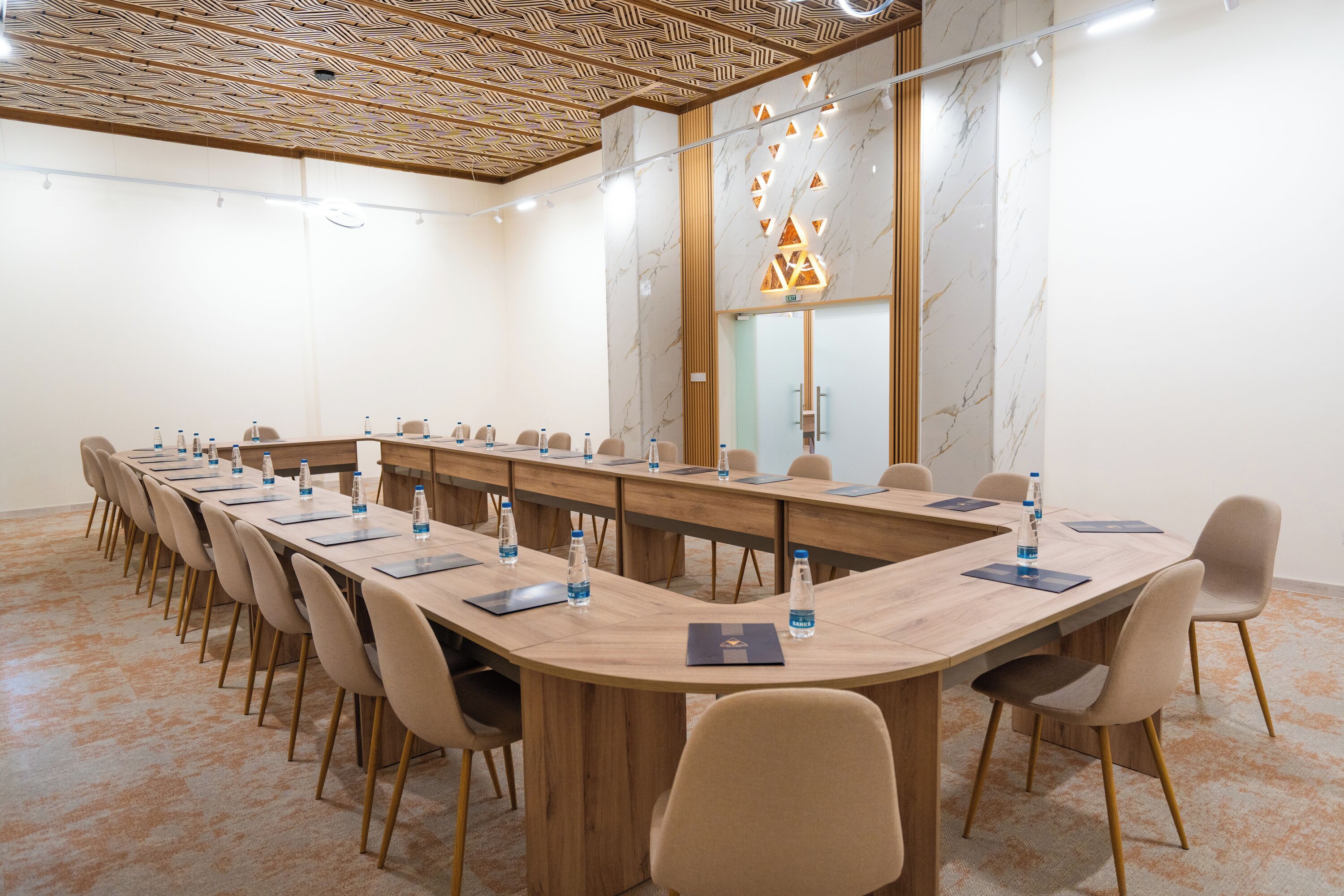 A conference room with a long table, chairs, water bottles, and a wooden ceiling.