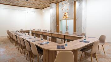 Een vergaderzaal met een lange tafel, stoelen, waterflesjes en een houten plafond.