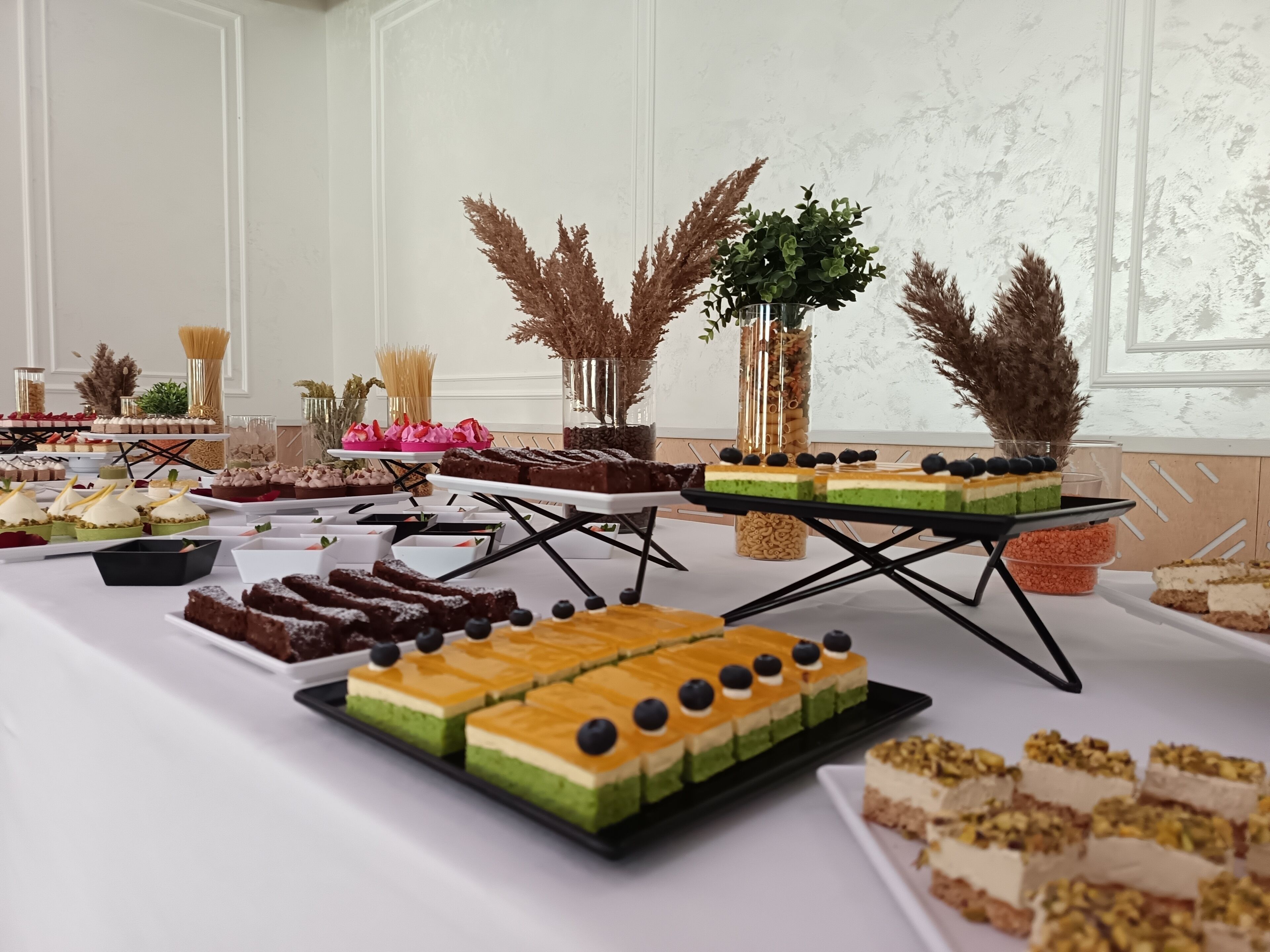 A buffet table with various desserts and a decorative arrangement of dried plants.