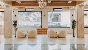Un lobby moderno con piso de mármol, mostrador de recepción de madera y tres sillones blancos.