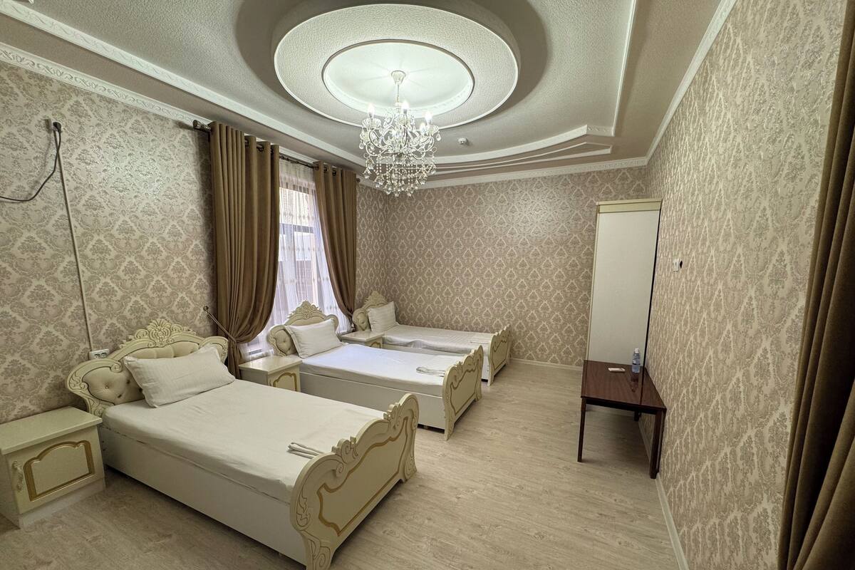 A hotel room with two beds, a chandelier, a mirror, and patterned wallpaper.