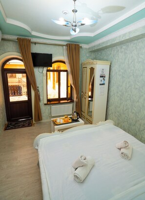 A hotel room with a bed, a mirror, a radiator, a window with curtains, a ceiling fan, and a door leading to an outdoor area.