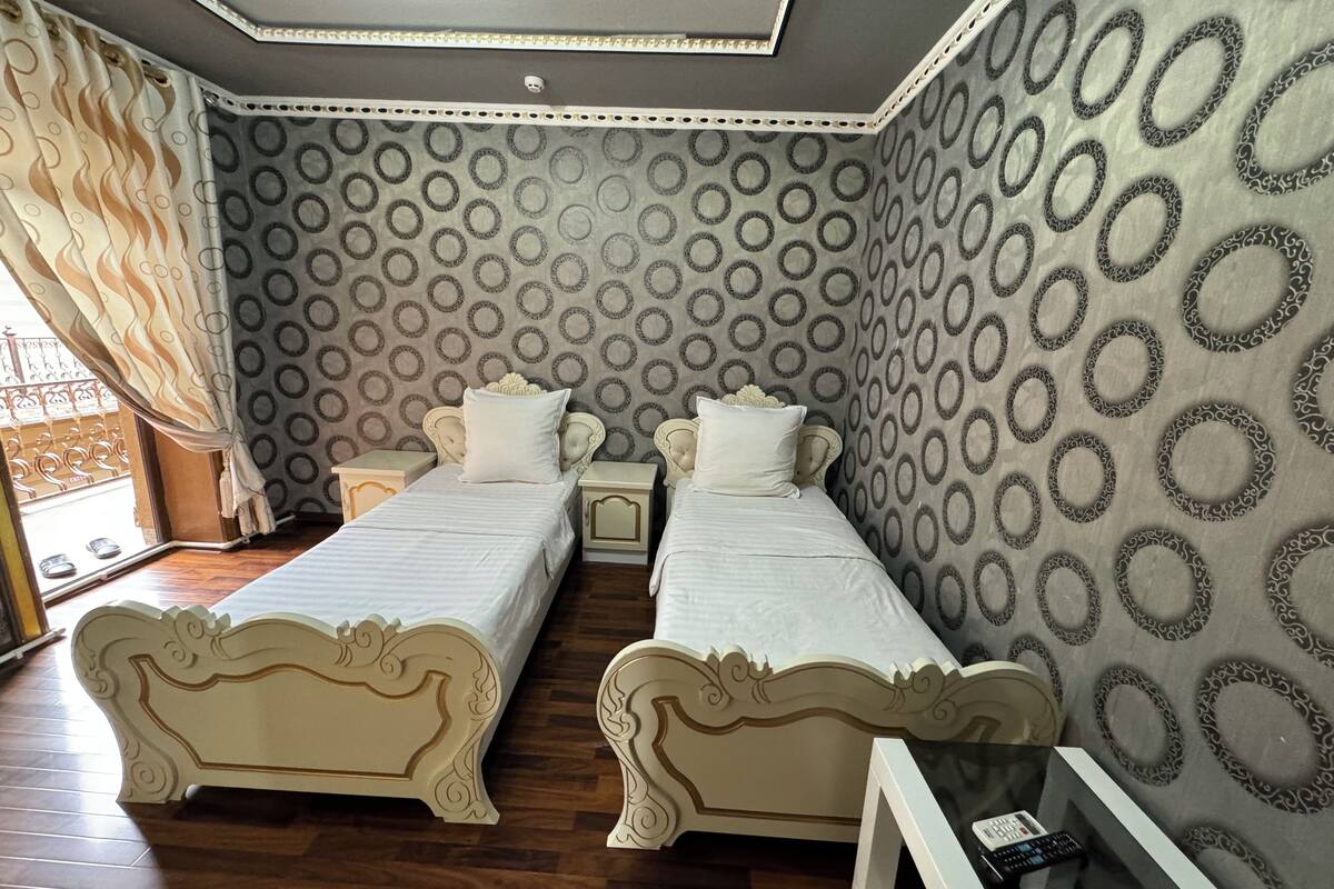 A room with two beds, a small table, and a patterned wall.