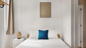 Ein Schlafzimmer mit einem großen Bett, einem Nachttisch, einem an der Wand befestigten abstrakten Kunstwerk und einer Holztür.