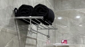 Ein Badezimmer mit einem Handtuchhalter, der zwei schwarze Handtücher trägt, einer kleinen Ablagefläche mit einem rosafarbenen Gegenstand und einer Marmorwand.