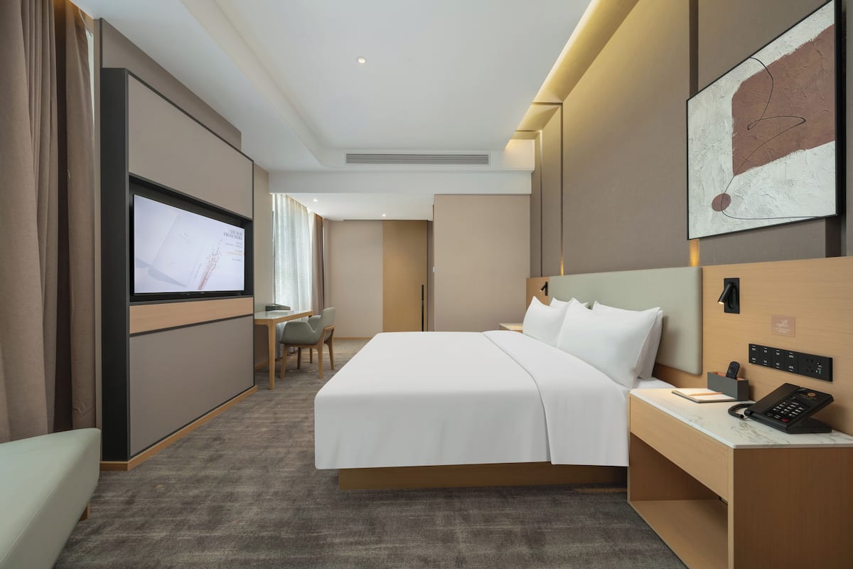 A hotel room with a bed, a desk with a phone, a TV, and a chair.