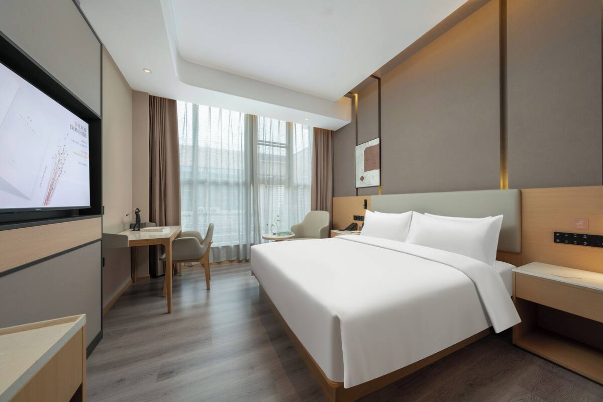 A hotel room with a large bed, a desk, a chair, and a TV.