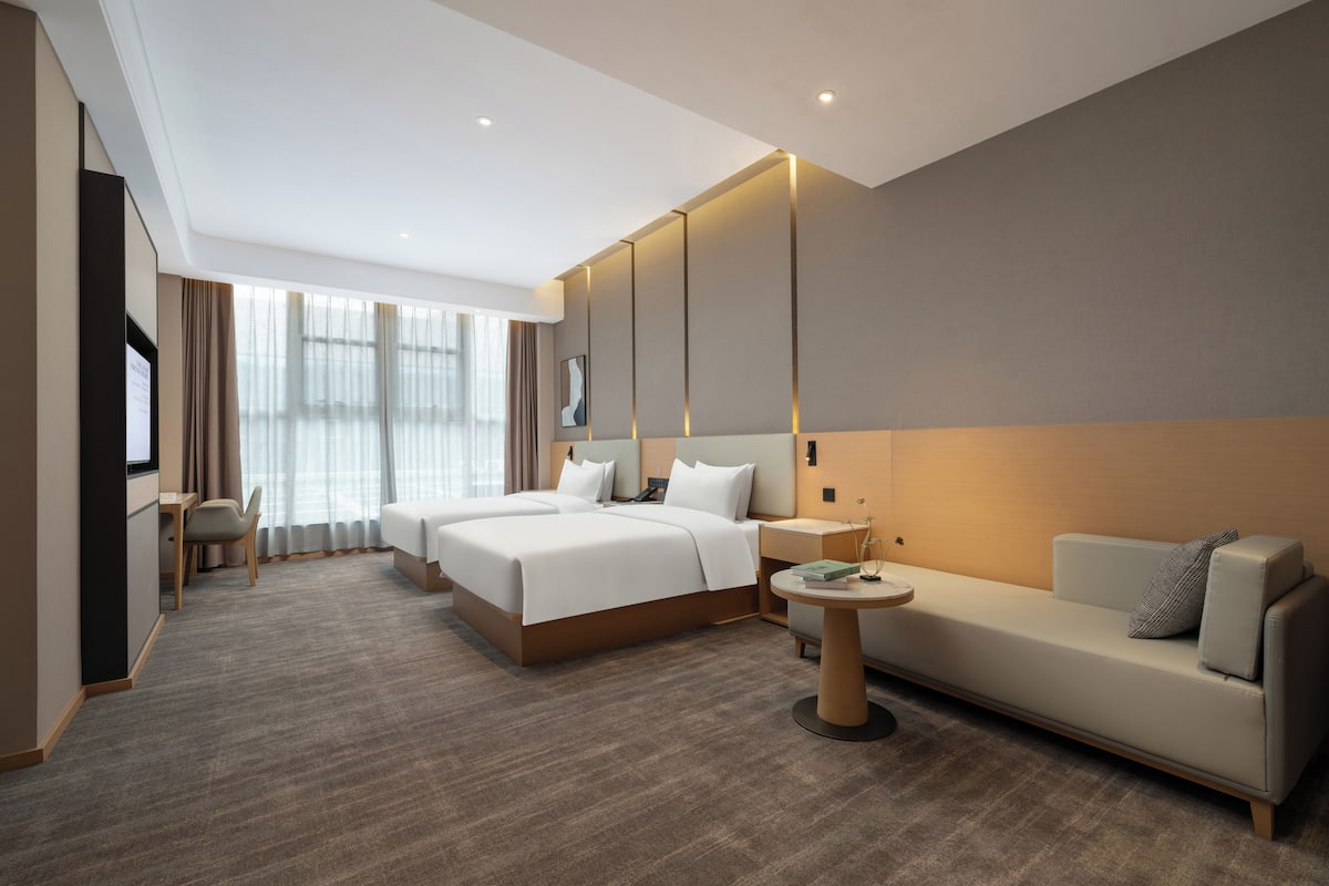 A modern hotel room with a large bed, a sofa, a desk, and a TV.