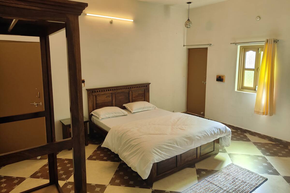 A bedroom with a bed, wooden headboard, a ceiling fan, a window with curtains, and a patterned floor.