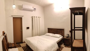 Un dormitorio con cama, un banco de madera, una mesita de noche con hervidor y una silla de madera.