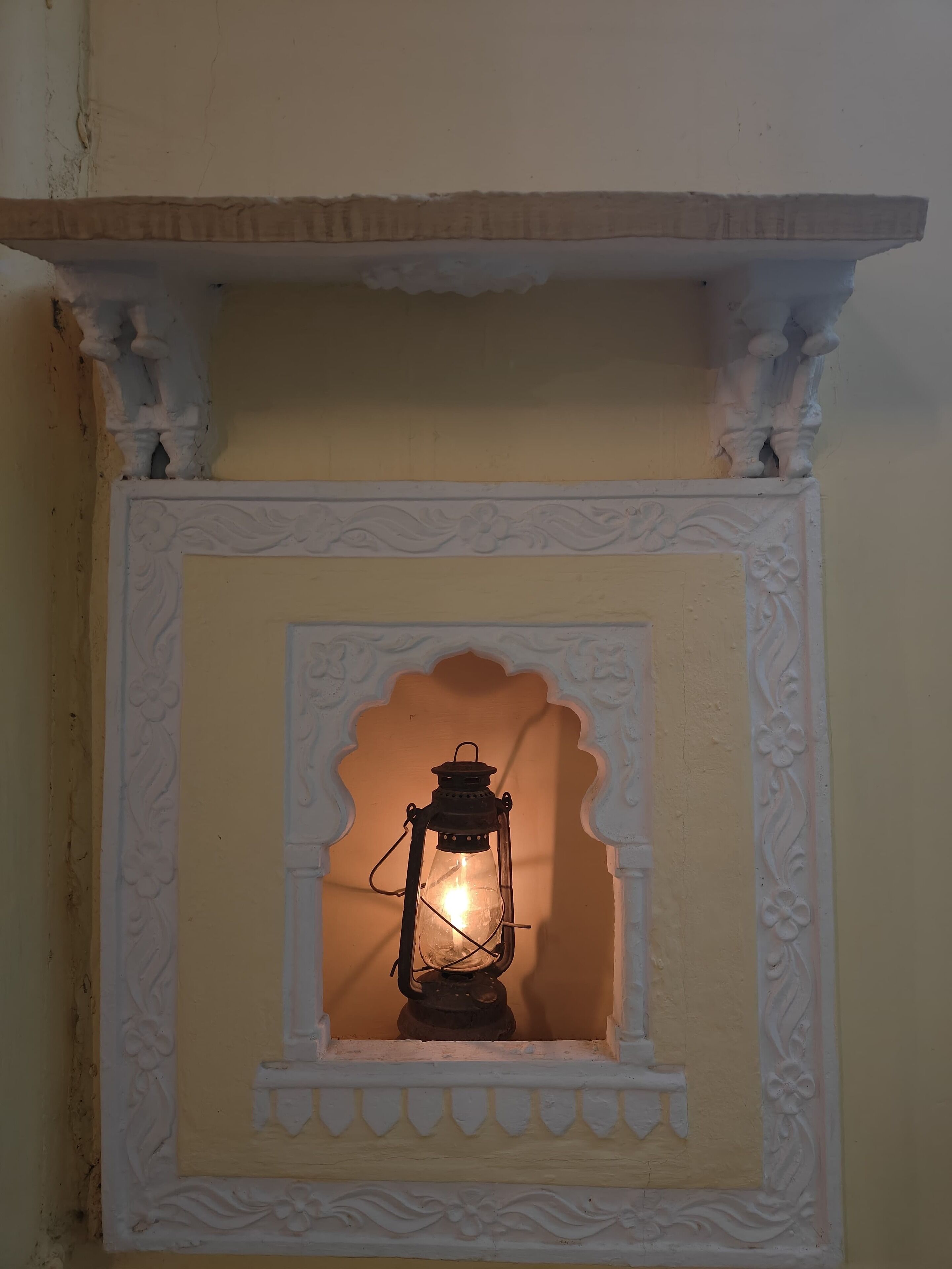 Een lantaarn in een decoratieve nis met versierde witte sculpturen.