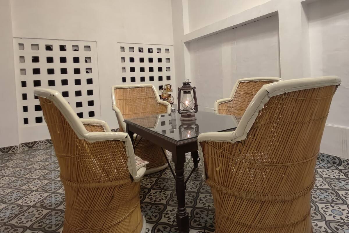 A room with a glass-top table surrounded by four wicker chairs, a lantern on the table, and patterned floor tiles.