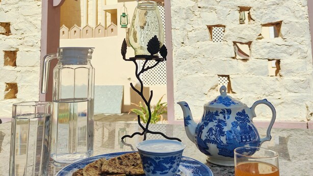 Una mesa servida con tetera, taza de té, jarra, vasos y pan plano.