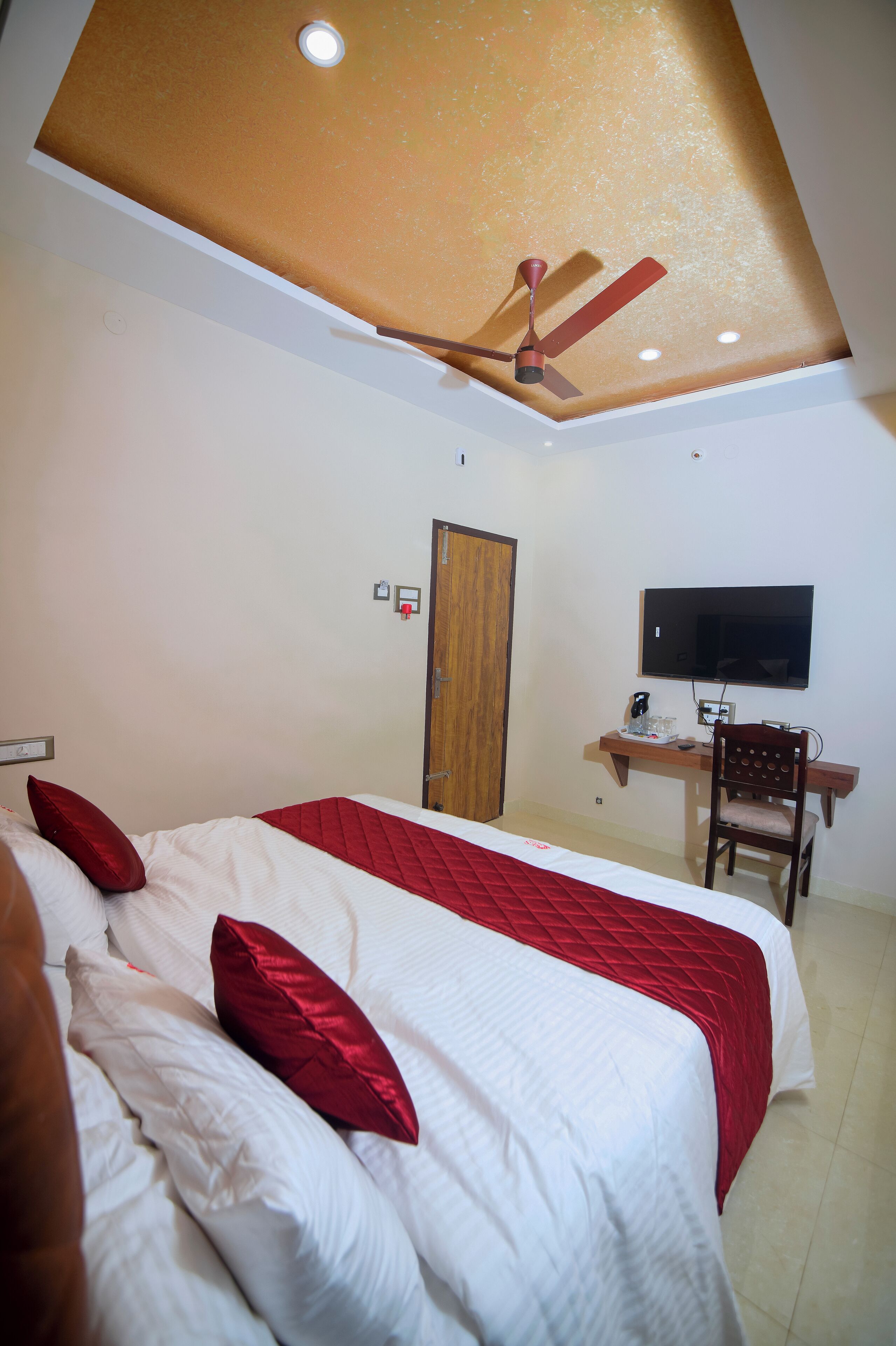 A hotel room with a bed, a desk with a chair, a television, and a ceiling fan.