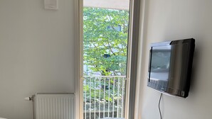 A bedroom with a bed, a radiator, a TV mounted on the wall, and a window with a view of greenery outside. - 2br on Tjuvholmen with sea view (Oslo)