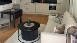 A modern living room with a sofa, a coffee table, and a TV. There is a kitchen area with cabinets and appliances. - 2br on Tjuvholmen with sea view (Oslo)