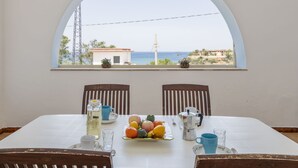 A dining table with chairs, a pitcher, a plate of fruit, and a view of the sea through an arched window. - Nice apartment for 6 people with A/C, WIFI, TV and terrace (Balestrate-foce)