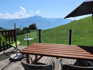 Une terrasse en bois avec une table et des chaises, offrant une vue sur un paysage verdoyant et des montagnes.