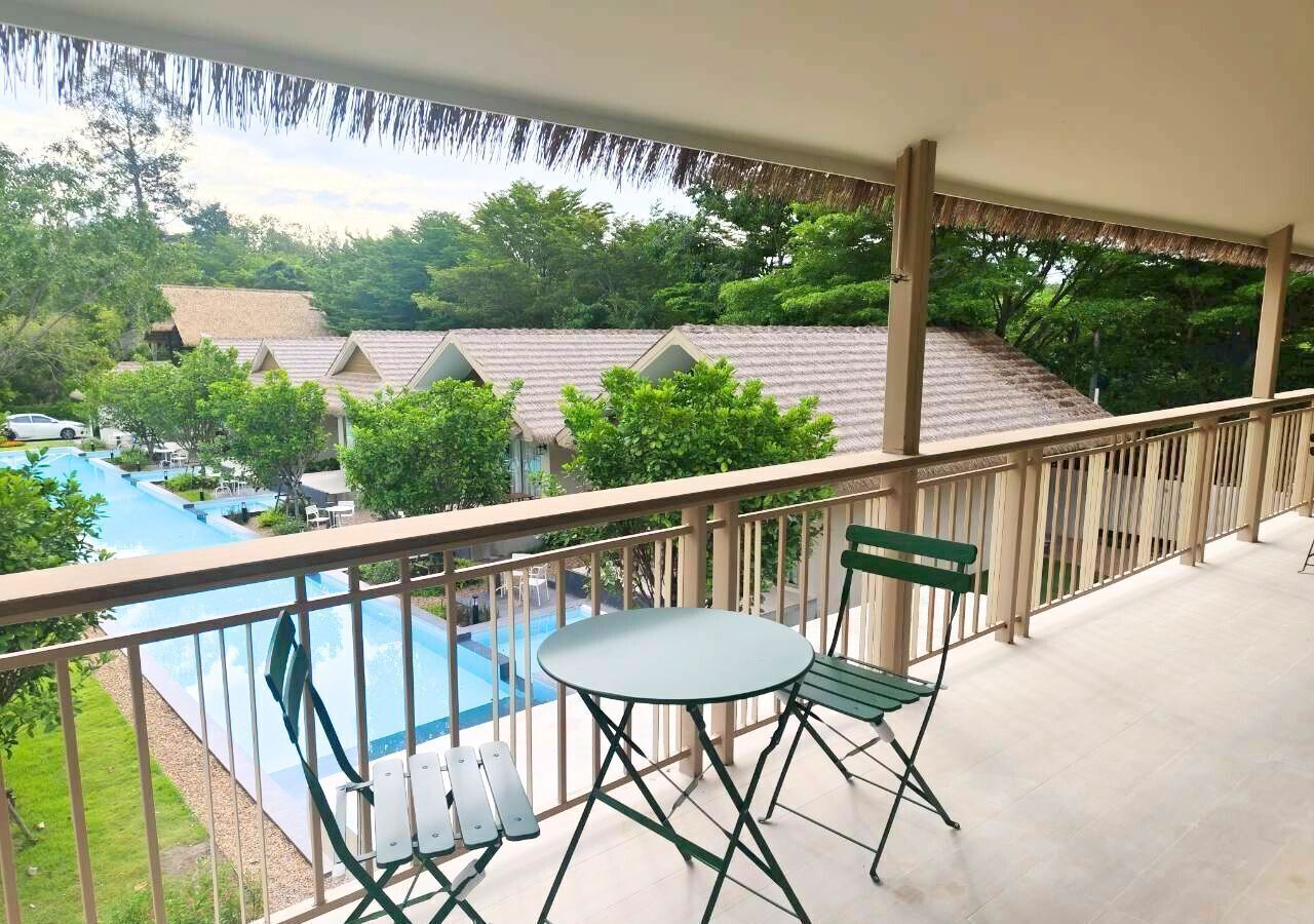 A balcony with a view of a swimming pool and a thatched roof building.