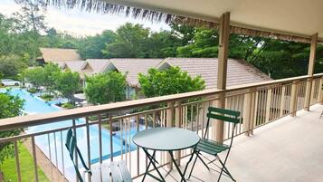 A balcony with a view of a swimming pool and a thatched roof building.